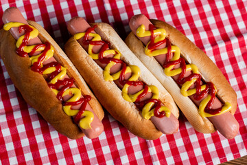 top view of delicious hot dogs with mustard and ketchup on plaid tablecloth