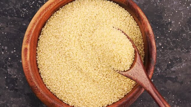 Raw couscous cereal seeds in wooden plate stir with eco friendly spoon on dark background