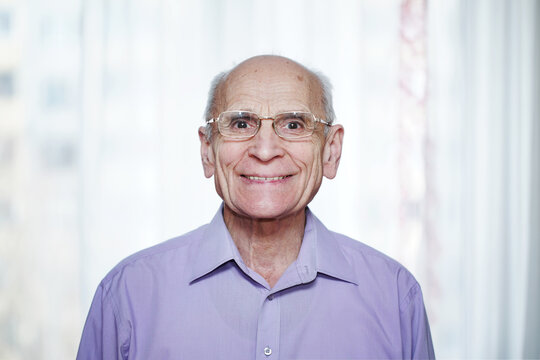 Close up portrait of happy senior man wearing eyeglasses against white curtain.