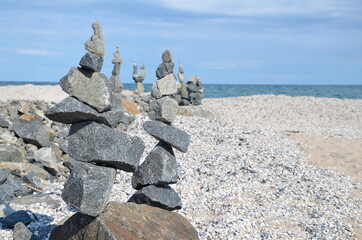 Close-up, tall figure of balancing stones on the seashore.
On the horizon are blue skies and small clouds.
