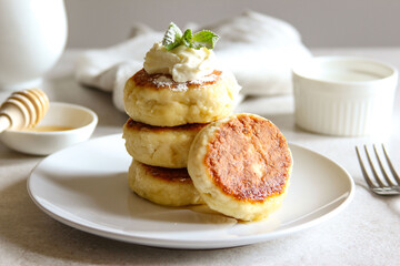 Sweet cheese pancakes with honey and cream on a white plate. Homemade recipe cheesecakes.