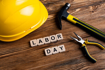 helmet, hammer, pliers and cubes with labor day lettering on wooden surface