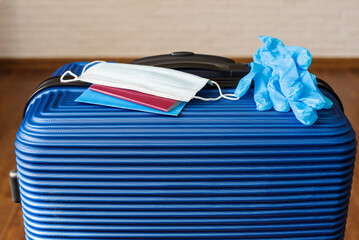 Blue suitcase for summer trip, during the coronavirus pandemic travel -protective mask, documents, vaccination certificate, hat. Reading for travel, travel bag in the hotel, arrived at the destination
