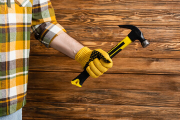 partial view of handyman in work glove holding hummer on wooden background, labor day concept - obrazy, fototapety, plakaty