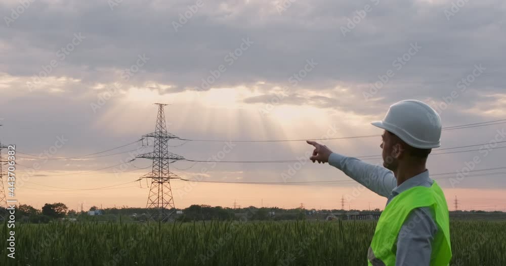 Wall mural an engineer looks towards a high-voltage power line and points at it with his index finger.