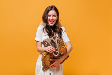 Cheerful girl posing with shopping bag full of fruits. Woman in white dress posing on orange background