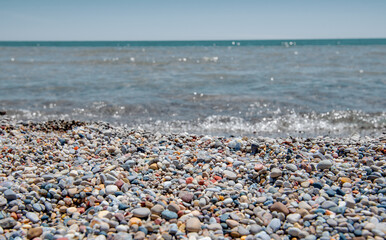 Colorful small seashells and pebbles on coastal beach with water background