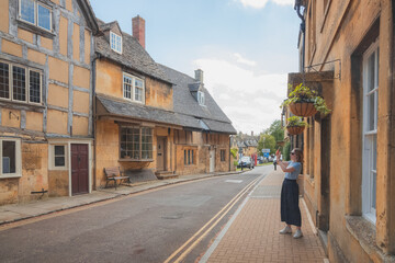 A young female tourist explores the charming, quaint English village of Chipping Campden on a sunny summer day in the Cotswolds, Gloucestershire, England.