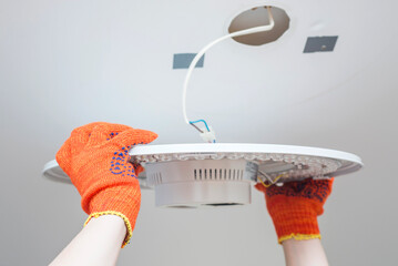 An electrician installs a chandelier on the ceiling. Hands of an electrician installing and...