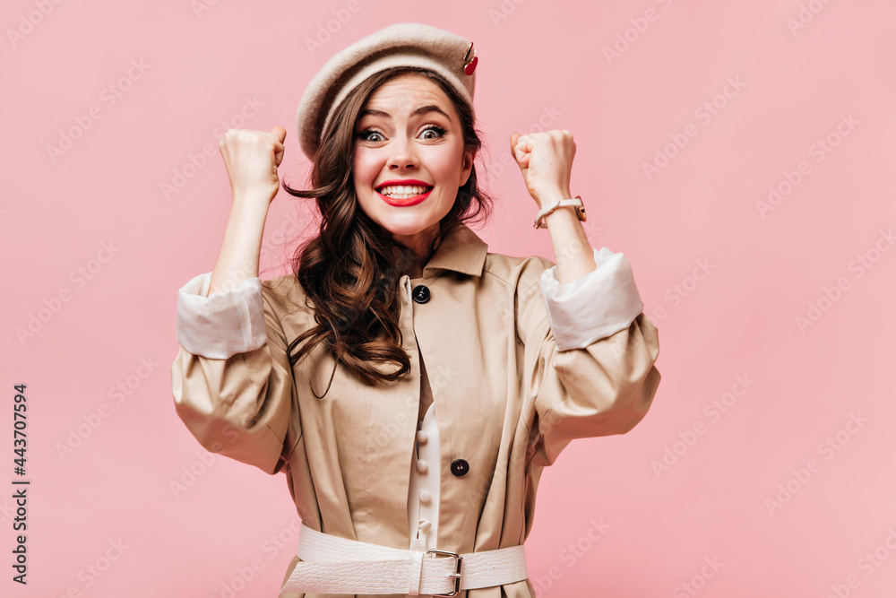 Sticker Woman in beige coat is happy with luck and looking at camera with smile on pink background