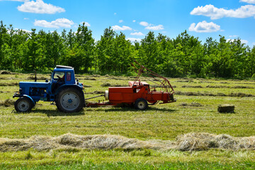 Fototapeta premium A tractor with a trailed bale machine collects the hay and bales it into windrows. Tractor with hay baler.