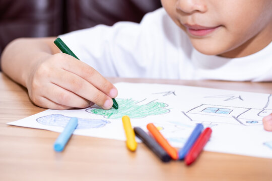 A little boy drawing a house with crayons is a beautiful imagination painting. A little child is engaged in creativity, the child does his homework.