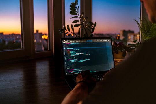 The code is on a laptop on a wooden table in front of the window  in the dark with a view of the lights of the night city, color lighting in the room, home decor	