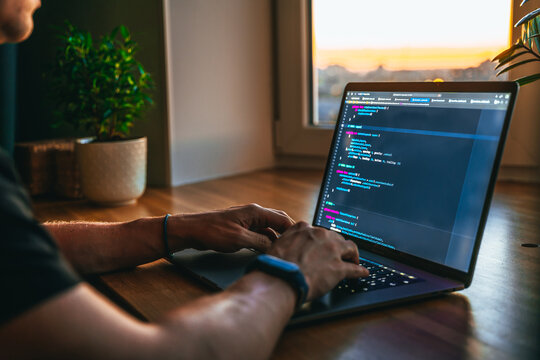 The code is on a laptop on a wooden table in front of the window  in the dark with a view of the lights of the night city, color lighting in the room, home decor	