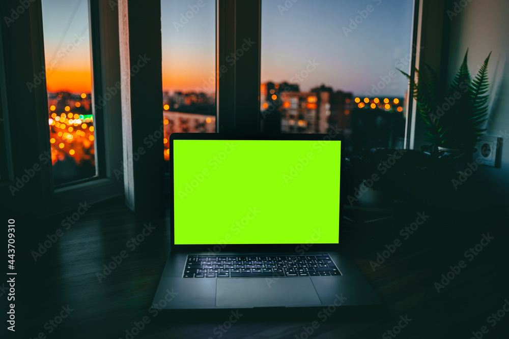 Canvas Prints a laptop with an empty green screen on a wooden table at night with a view of the city with colored 