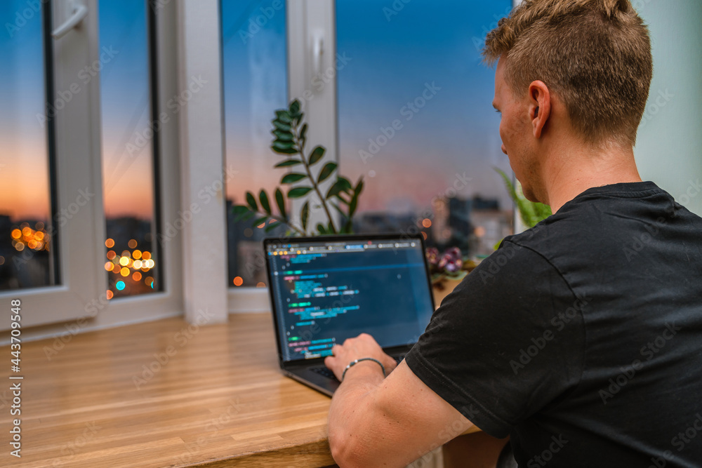 Canvas Prints a young male developer is programming a code script late at night with beautiful city lights at nigh