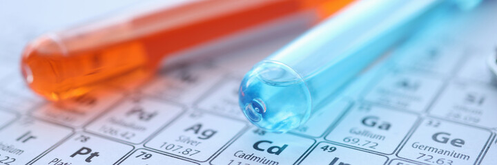 Two test tubes with colored reagents lying on periodic table closeup