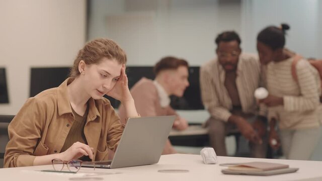 Medium shot of young female IT student being bullied in class Girl trying to study on laptop while classmates throwing crumpled pieces of paper at her