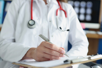 Doctor writing in medical documents on clipboard in clinic closeup
