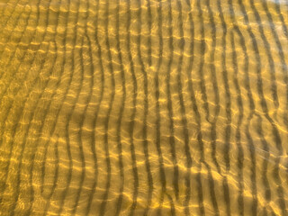 The rippled sandy seabed in a shallow bay under the sun's rays creates an unusual structure and pattern. The golden sands of the Baltic coast of the resort of Narva in Estonia.  Close-up pattern