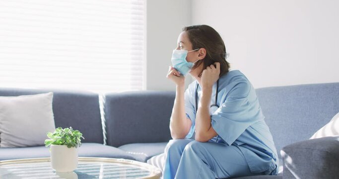 Caucasian female doctor wearing face mask at home sitting on couch