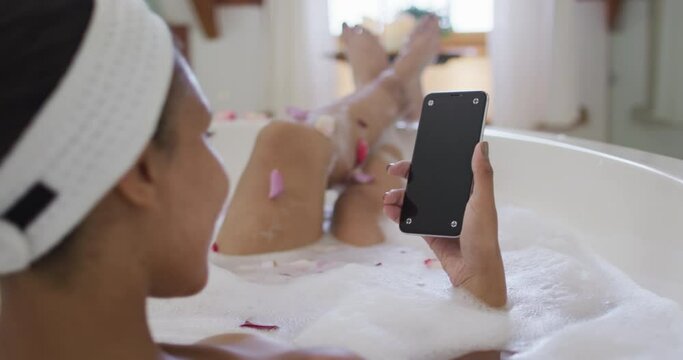 Mixed race woman taking a bath and using smartphone