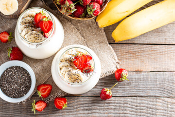 Dessert with yogurt, strawberries, banana, chia seeds, served in glass jars on a table, delicious dessert for healthy breakfast. Top view