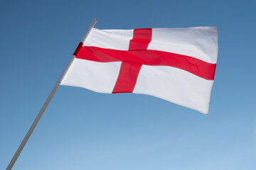 English flag waving in wind. Flag of England on blue sky background.