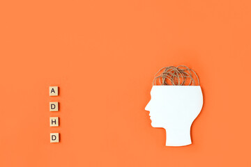 Silhouette of human head, tangled threads and wooden blocks with letters ADHD on orange background....