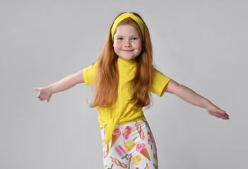 Studio shot fun little red-haired girl in a summer dress fashion, which spread his hands, flying like an airplane. Happy vacation holiday moments and sincere childish emotions concept