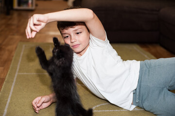 a boy plays with a black kitten at home
