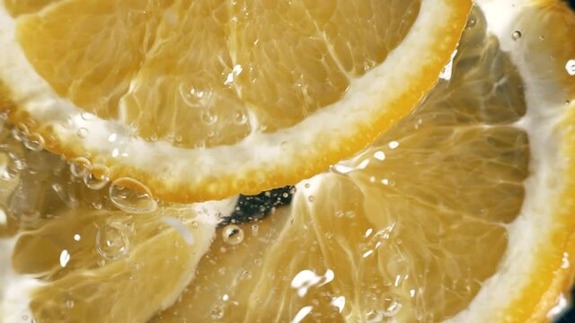 Orange slices are falling into a water in slow motion. Water splashing on fresh orange. Water dropping from citrus fruit. Close up orange slice rich in vitamin C.