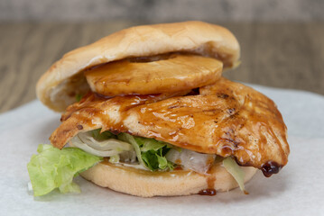 Full breast of chicken dripping under the pineapple ring of the huge teriyaki chicken burger sandwich.