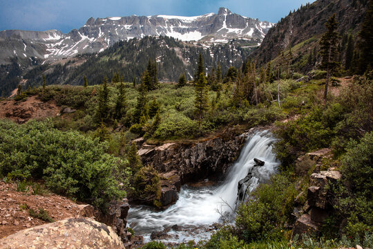 View of a waterfall surrounded by greenery, mountains, and trees in Yankee Boy Basin near Ouray, Colorado. 
