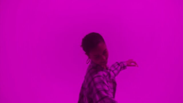 Attractive talented woman dancing hip hop on purple neon background in studio. Shooting of modern choreography for advertising of dance school, dancer expressing feelings for music video performance.