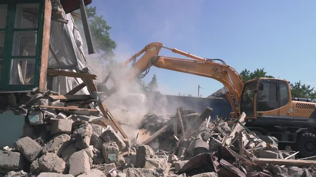 Excavator bucket loads trash and debris from destroyed building into truck. Demolition of house.