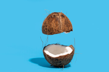 Coconut split on half with one half floating in air. Blue background. Creative food concept 
