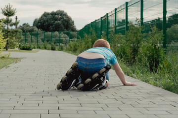 A boy tries to get up from the ground after falling with the roller skates. a boy riding a bike or...