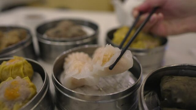 This video shows chop sticks pick up a fresh shrimp ha gow from a restaurant table filled with delicious dim sum.