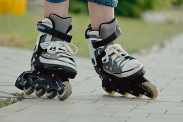 Little boy in protective equipment and rollers stands on walkway in park, low angle view