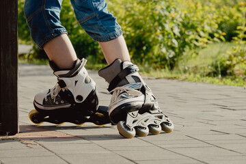 Little boy in protective equipment and rollers stands on walkway in park, low angle view