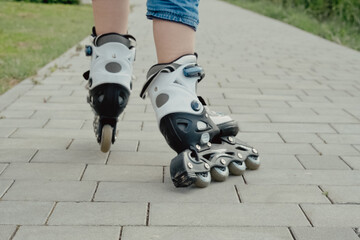 Little boy in protective equipment and rollers stands on walkway in park, low angle view