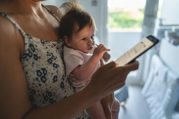 Adult woman mother holding three months old baby while using looking mobile phone for internet browsing or social network texting in room at home domestic life motherhood and parenting busy concept - Powered by Adobe