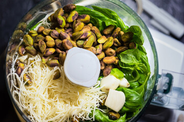 Overhead image in food processor of pesto ingredients, basil, parmesan, lemon, pistachio, olive oil, and garlic cloves. Bright green and yellow ready to make this genovese sauce from Italy for pasta.