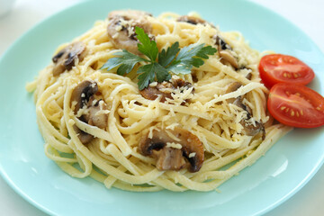 Italian fettuccine pasta with mushrooms and cream sauce, sprinkled with cheese, garnished with tomatoes and parsley in a blue plate. Close-up. Selective focus.