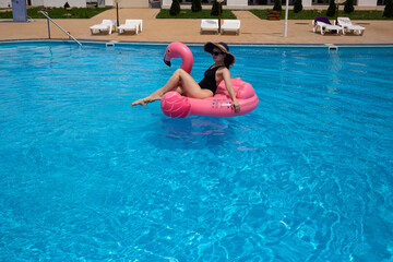 Naklejka premium Beautiful woman on flamingo pool float in pool. Summer holidays