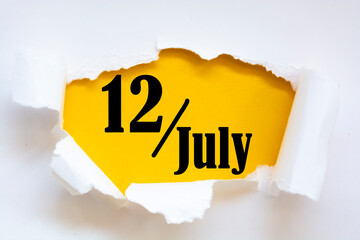 July 12. 12th day of the month, calendar date. Hole in paper with edges torn off. Yellow background is visible through ragged hole. Summer month, day of the year concept.