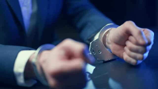 Arrested criminal businessman in handcuffs in the interrogation room. Arrest of the offender. Detention and interrogation of the accused man.