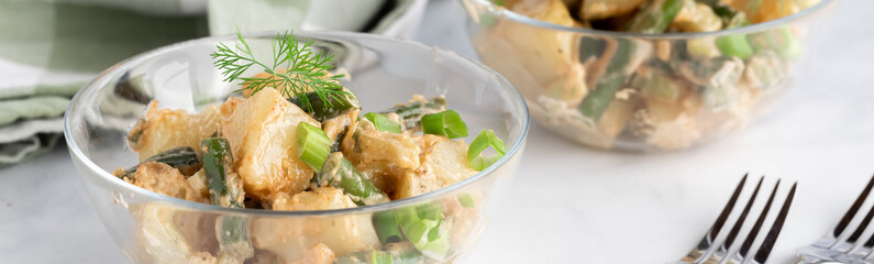 Narrow view of a bowl of a potato salad with another in soft focus in behind.