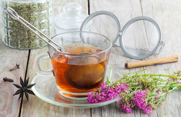 Red Valerian tea in a cup with a strainer over a wooden table with some props on it